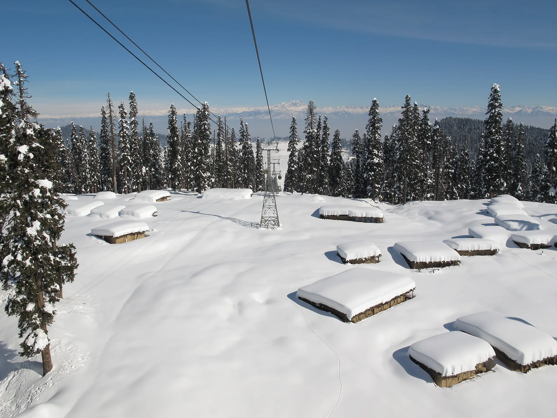 Gulmarg Gondola cables above snow-covered huts and pines