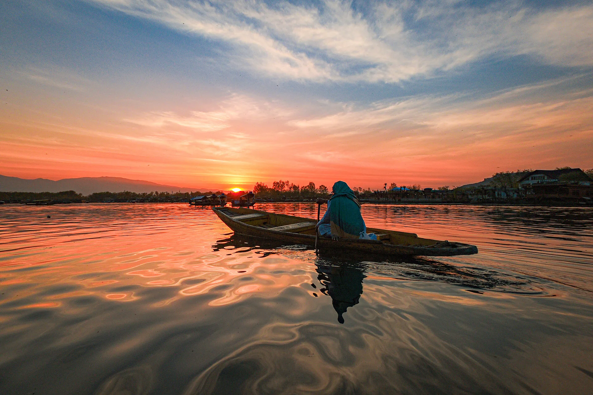A shikara silhouetted on Dal Lake at sunset